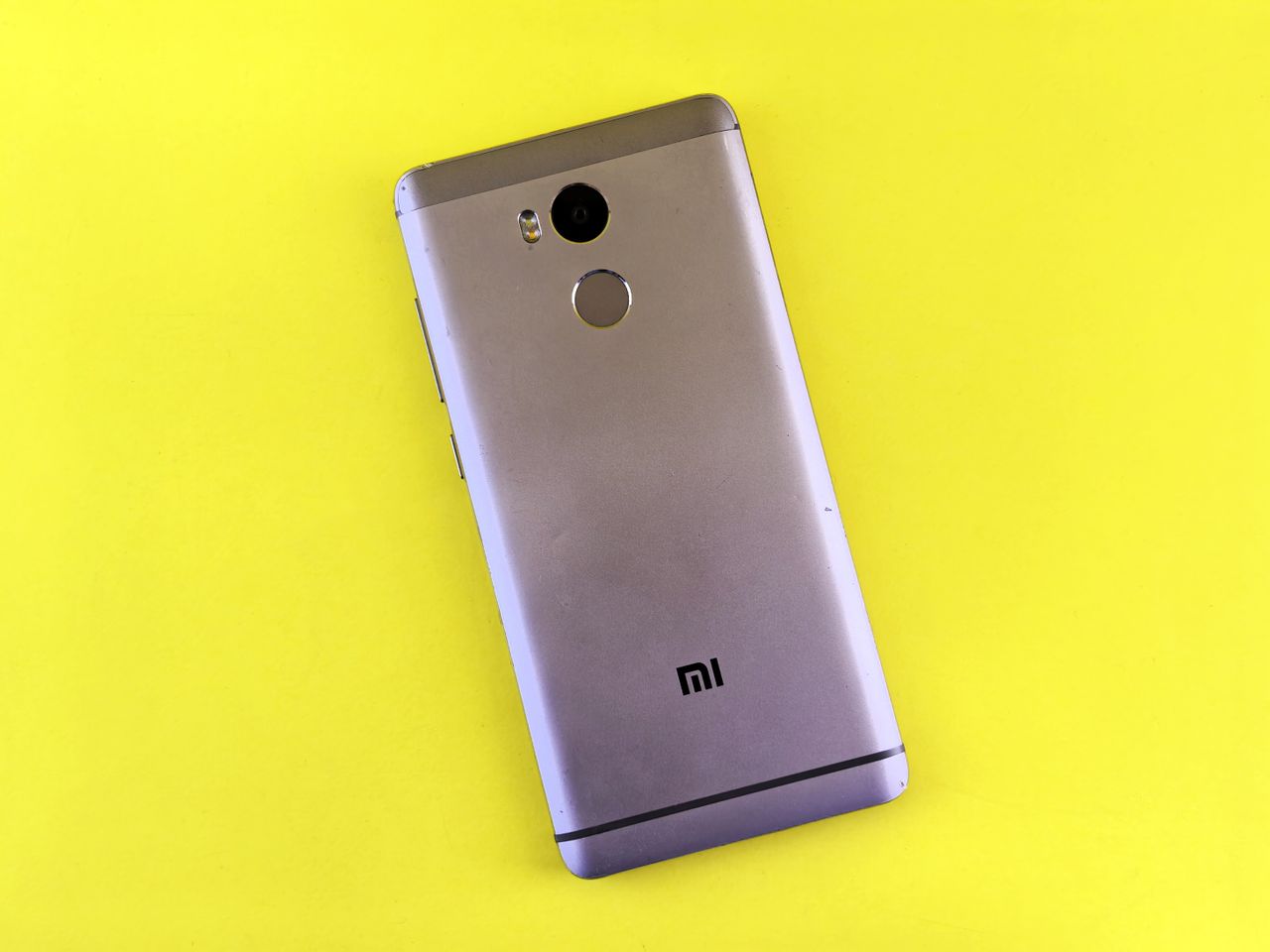 A silver smartphone placed on a bright yellow background, showcasing sleek design.